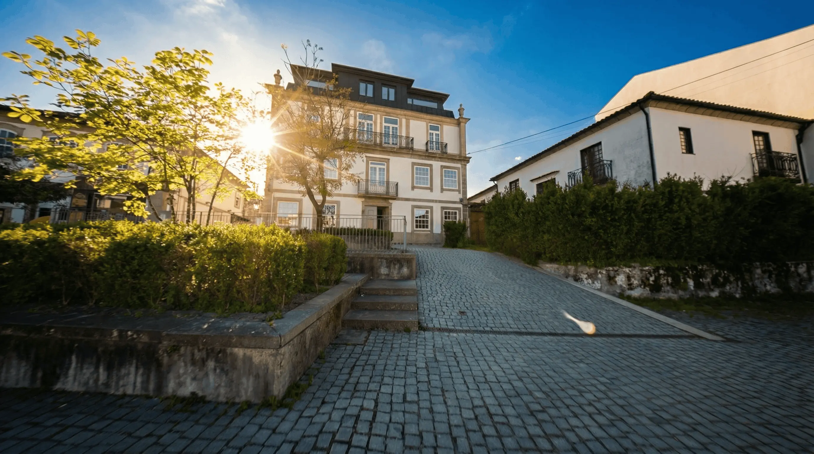 Palacete em Santo Tirso ao final do dia, com a luz do sol entre as árvores e acesso em calçada